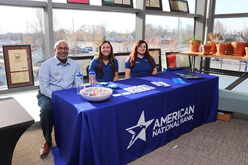 A man and 2 women sitting behind an American National Bank event table